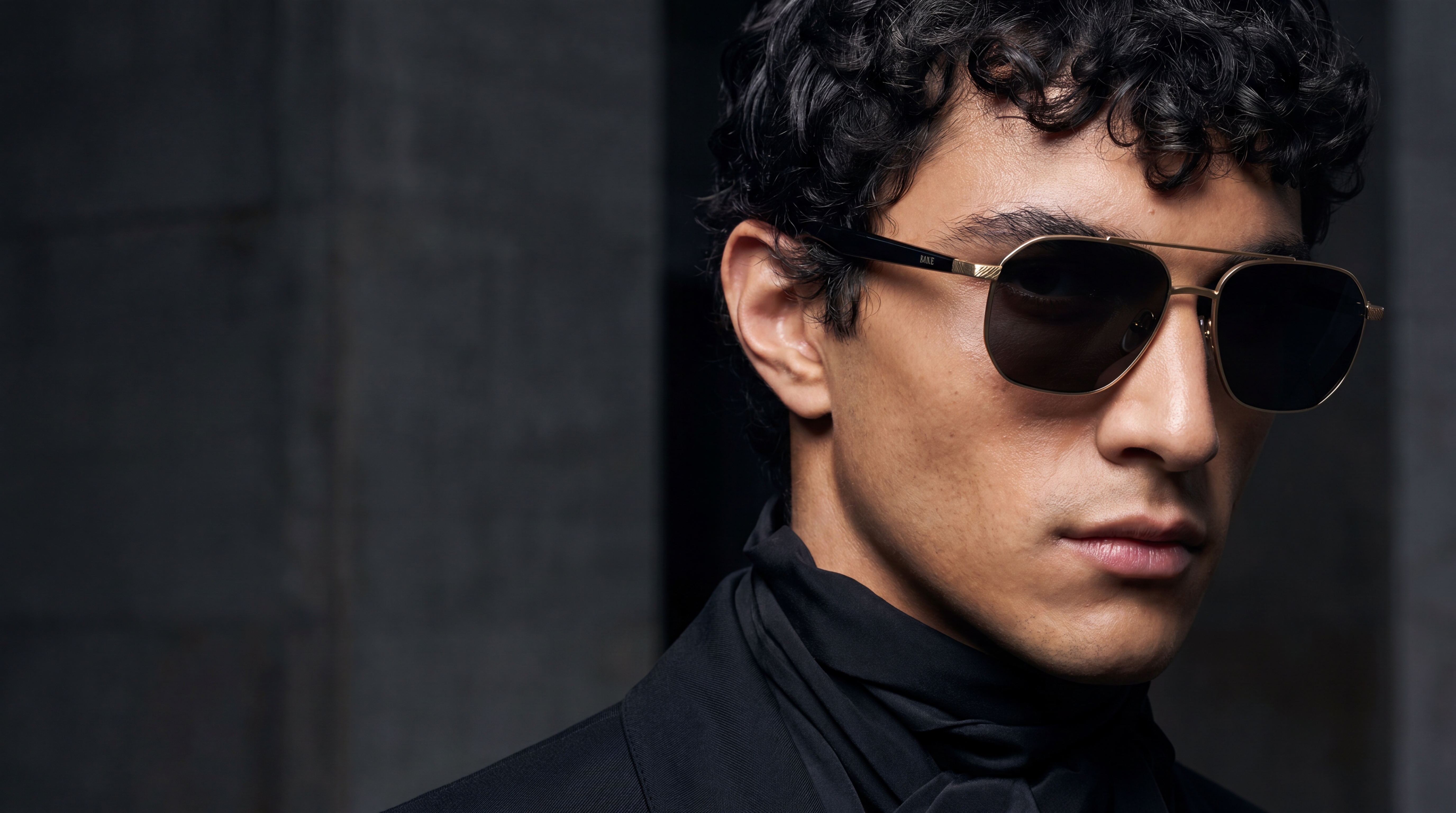 Model wearing pale gold sunglasses in a dark architectural setting